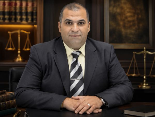 Confident lawyer in suit sitting at desk with legal books and scales of justice.