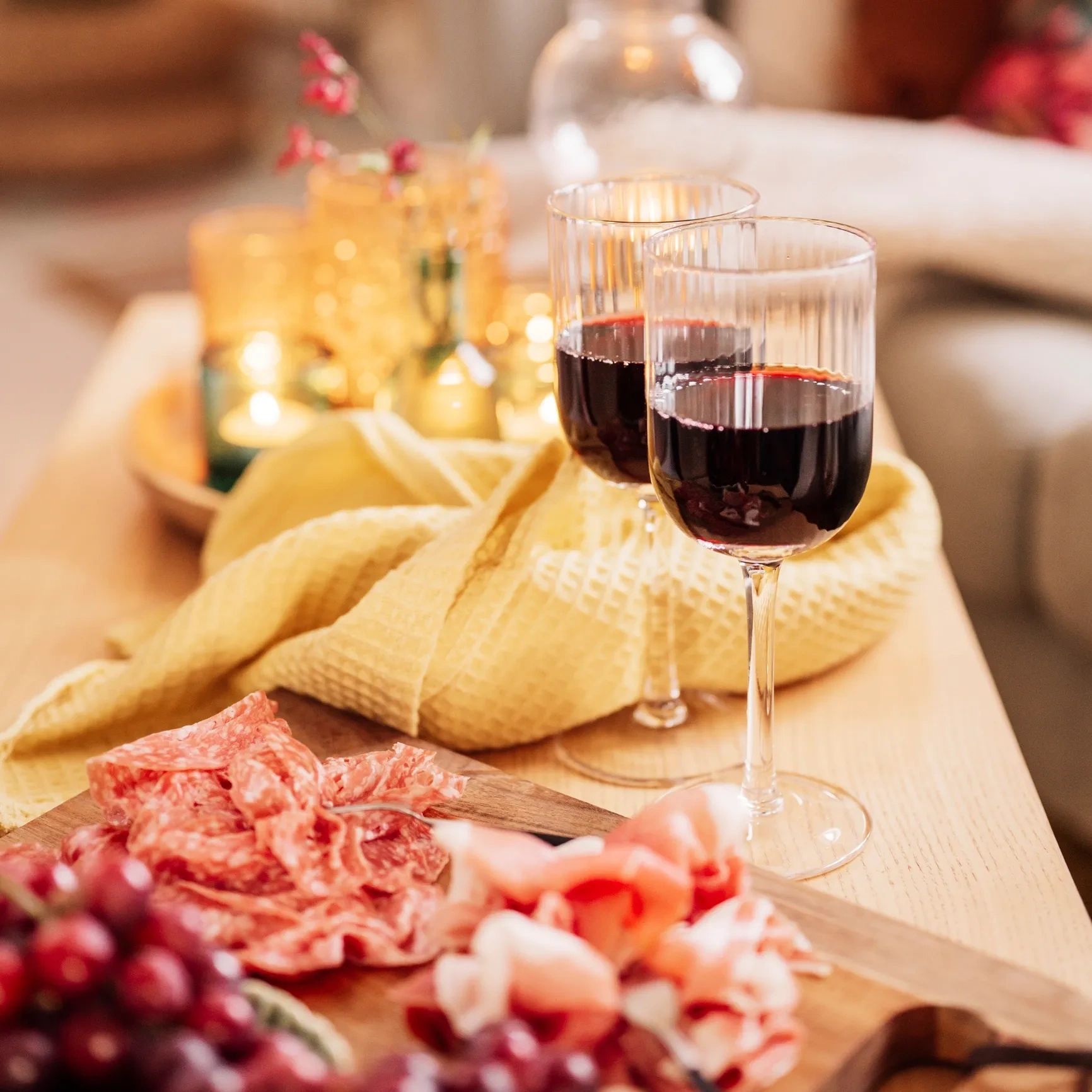 Two glasses of red wine with a charcuterie board and cozy yellow cloth.