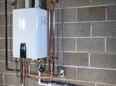 Tankless water heater installed on a concrete wall with copper piping.