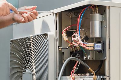 Technician fixing an air conditioning unit with open panel showing wires.