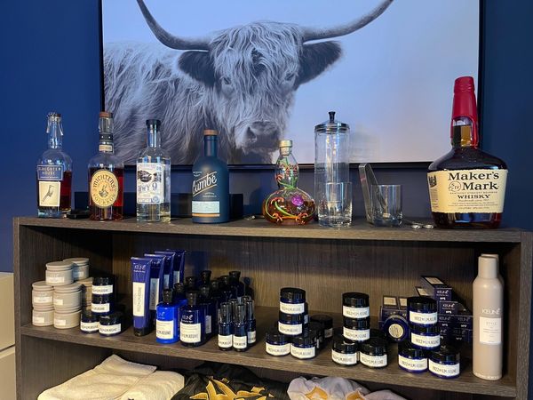 A shelf displaying various alcohol bottles and blue beauty products, with a large cow photo above.