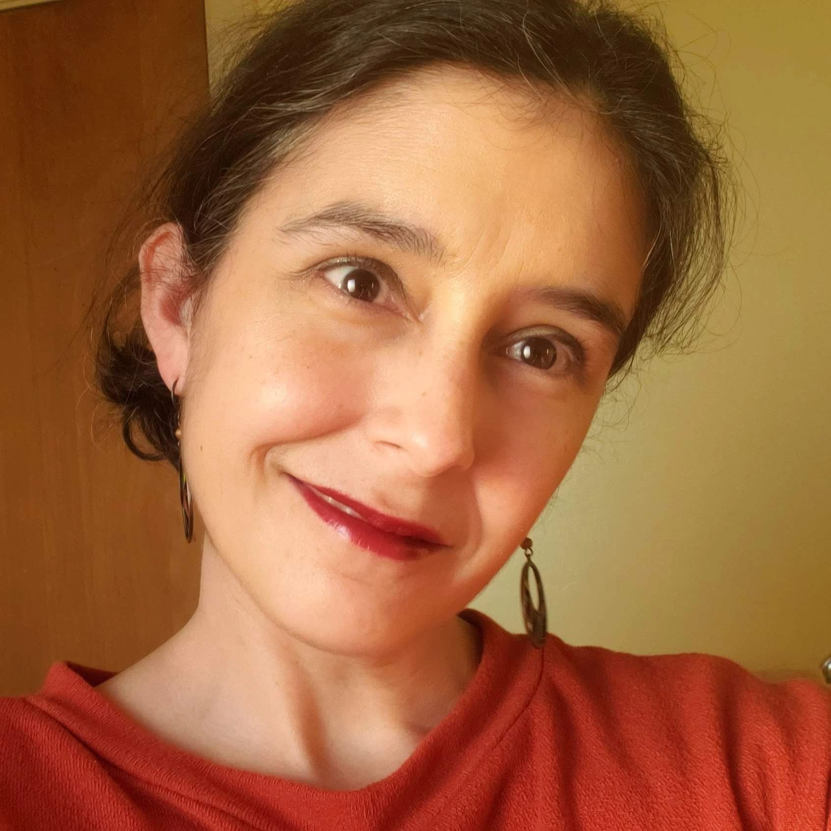 Michelle's face and shoulders, they have dark hair, bold lipstick, and dangly earrings.