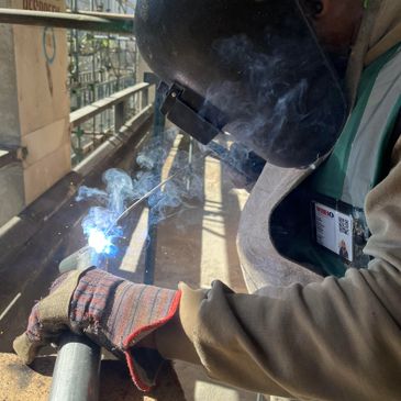 A welder wearing protective gear welds a metal pipe, emitting bright sparks and smoke.