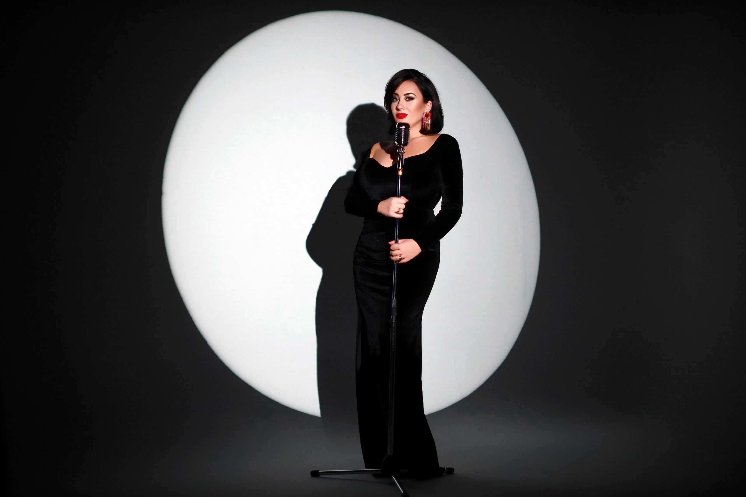Woman in black dress singing into a vintage microphone spotlighted on stage.