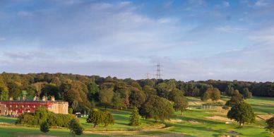 A scenic golf course with trees and buildings under a partly cloudy sky.