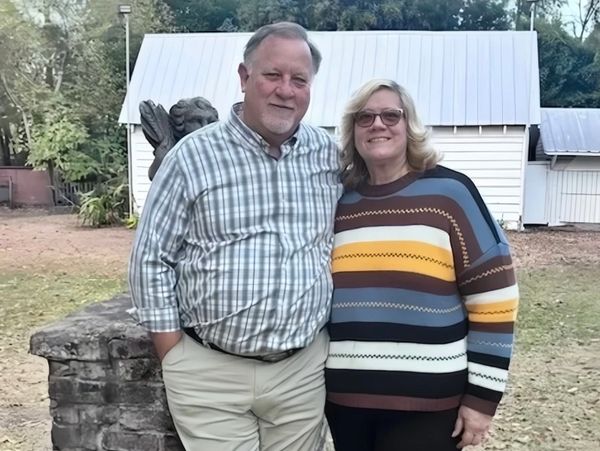 A smiling couple posing outdoors in front of a white shed.