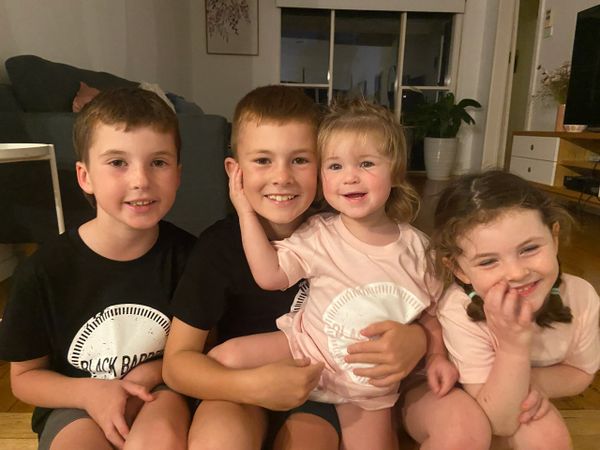 Four happy children sitting closely together, smiling at the camera indoors.