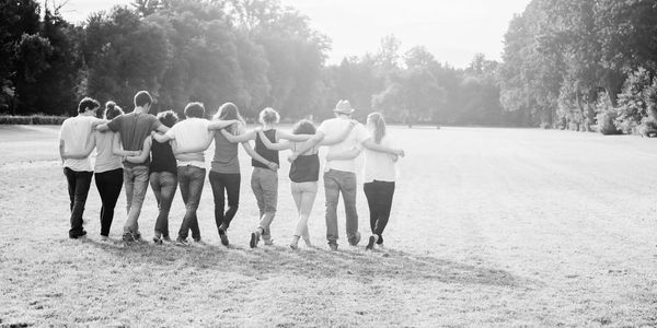 diverse group of ten friends walking towards a sunset together with arms around eachother