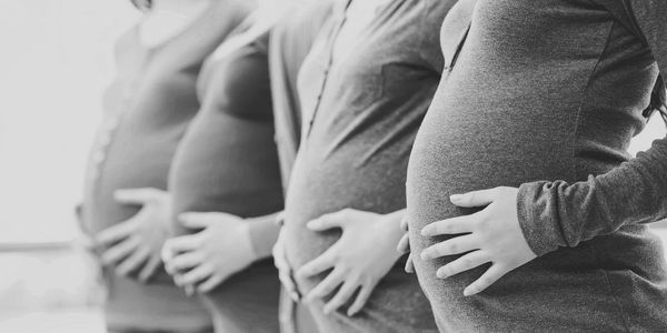A group of pregnant women gather for a picture of their belly bumps.