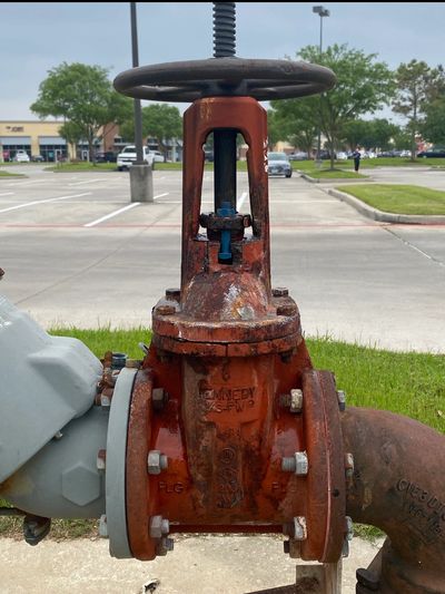 Rusty red valve with a wheel handle in a parking lot.
