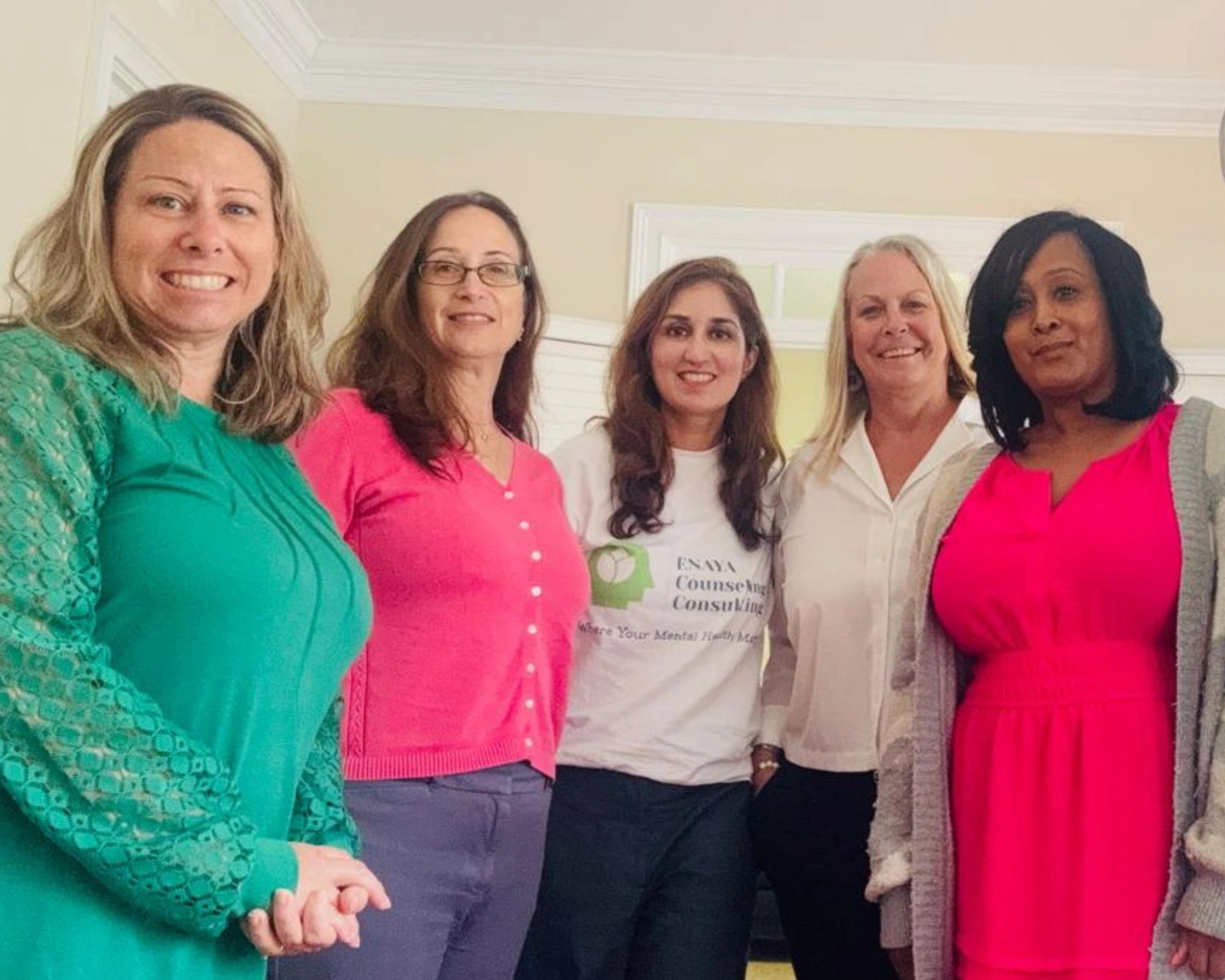Five women standing together indoors, smiling.