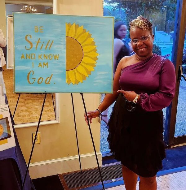 Woman in purple dress posing next to a sunflower painting with a spiritual quote.