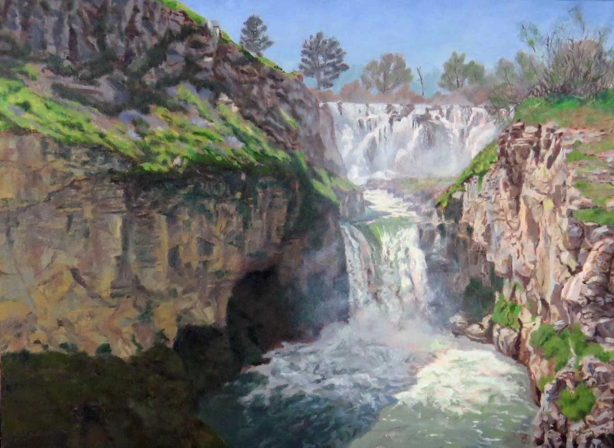 A cascading waterfall surrounded by rocky cliffs and greenery.