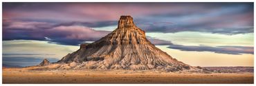 A solitary mesa under a colorful sky in a desert landscape.