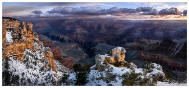 Snow-dusted cliffs overlooking the vast Grand Canyon at sunset.