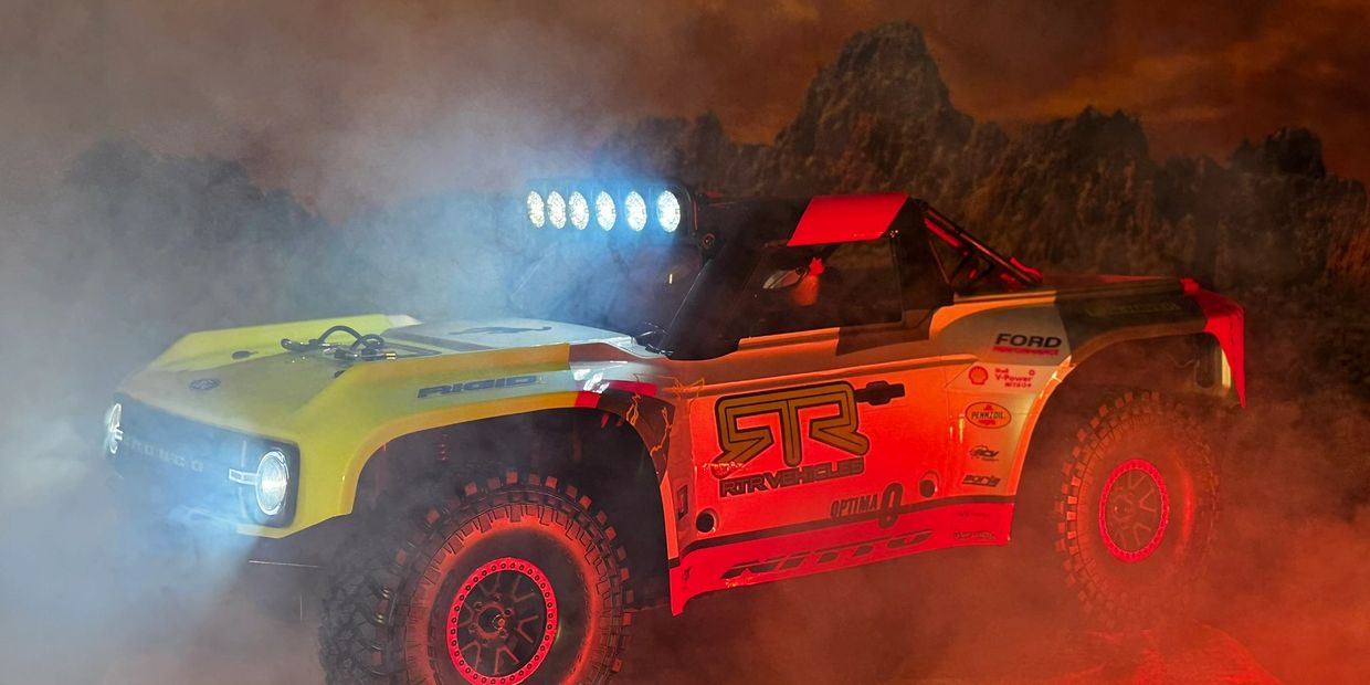 Off-road racing truck with bright lights in smoky, mountainous terrain.