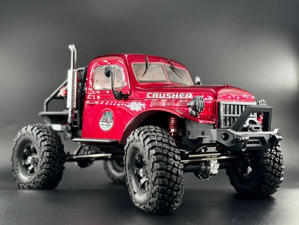 Red off-road RC truck with large tires on a dark background.