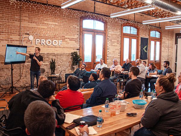A man presents to a group in a rustic office with exposed brick walls.