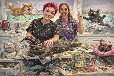 Two cheerful groomers styling a large fluffy cat amid playful cat illustrations.