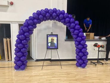 Purple balloon arch with a framed photo in a gym.