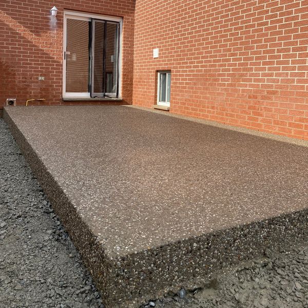 Newly poured exposed aggregate concrete patio behind a brick house.