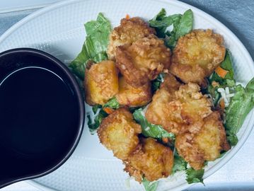 Plate of crispy fried chicken bites with dipping sauce on lettuce.