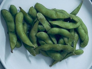 Fresh green edamame pods on a white plate.