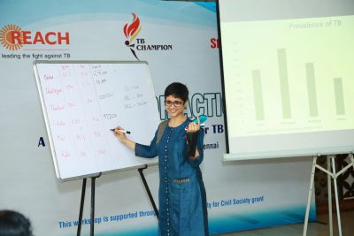 Woman presenting TB statistics with a whiteboard and projector.
