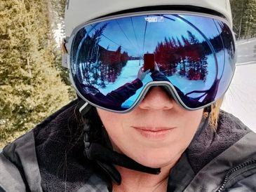 Close-up of a person wearing ski goggles reflecting a snowy forest.