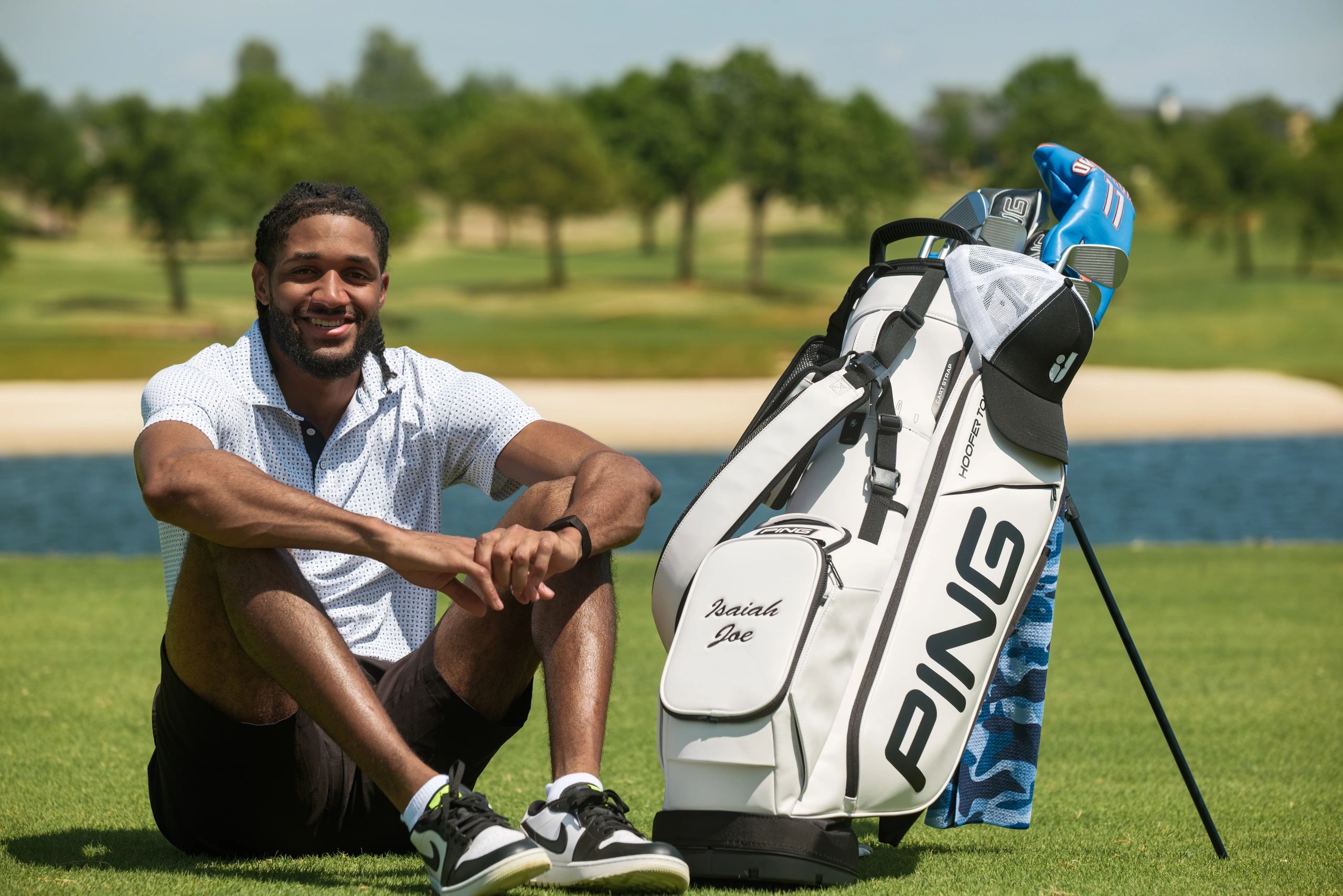Smiling man sitting on grass near golf bag on a sunny day.