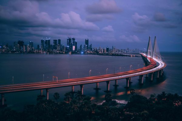 A city skyline with a curved bridge lit up at night over water.