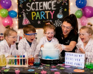 Children and teacher excited at a colorful science party with experiments.