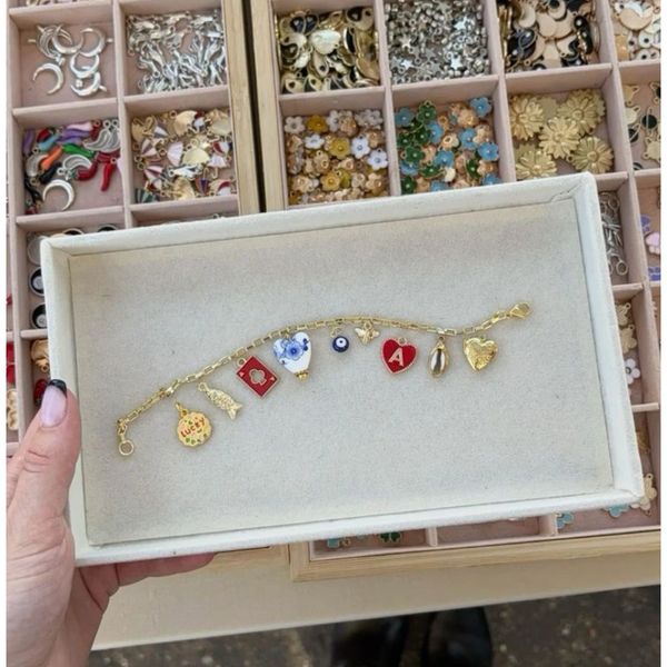 Gold charm bracelet with various colorful and symbolic charms displayed in a box.
