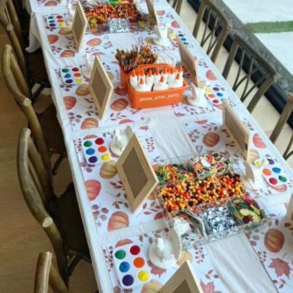 Table set for a kids' art and craft party with paints, glue, and decorations.
