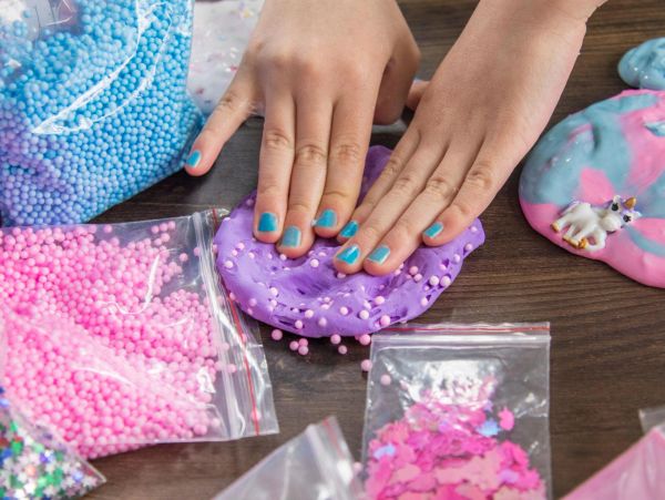 Hands playing with purple slime and foam beads.