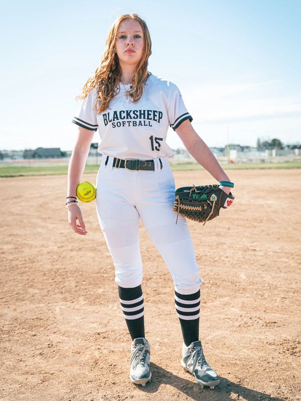Female softball player in uniform holding a glove and ball.