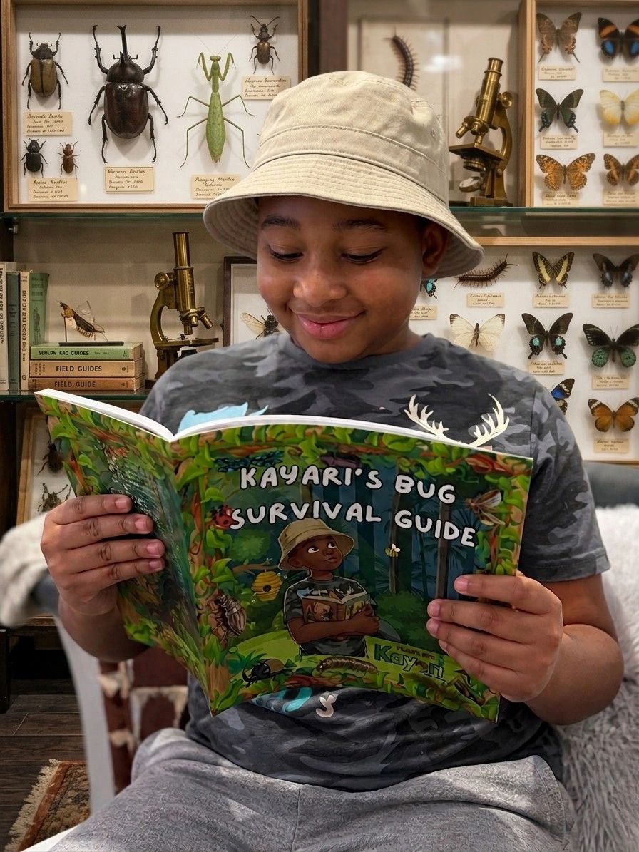 A boy in a bucket hat reads a colorful bug survival guide book.