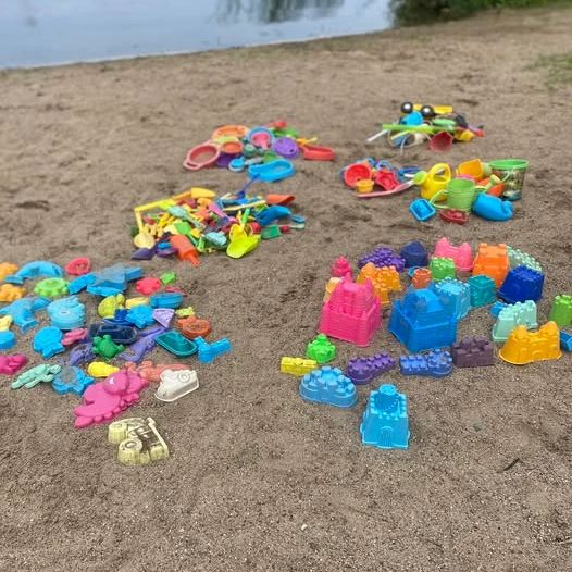 Colorful plastic sand toys arranged on a sandy beach near water.