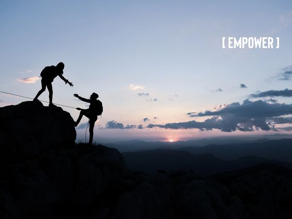 Two silhouetted climbers assist each other on a rocky ledge against a colorful sunset backdrop, symbolizing empowerment.