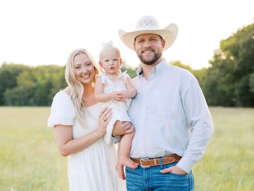 A family of three posing outdoors in a sunny field.