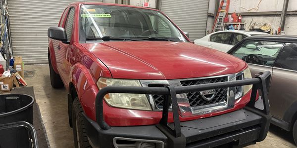 Red Nissan pickup truck with a sturdy front bumper inside a garage.