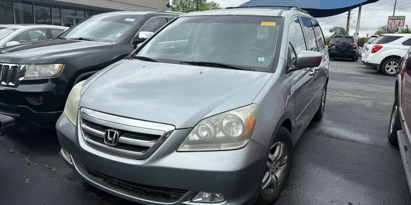 Silver Honda minivan parked in a lot with other vehicles.
