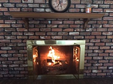 A cozy brick fireplace with a burning fire and a clock above it.