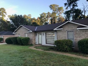 Single-story brick house with a front lawn and bushes.