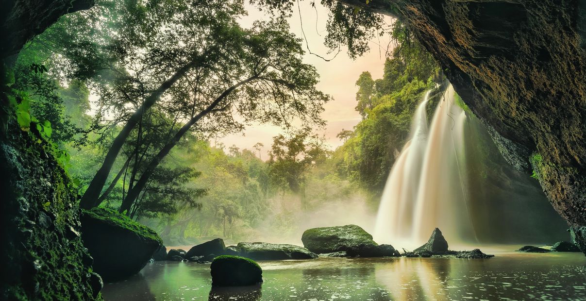 A serene waterfall flowing into a misty river, framed by lush green trees and rocks.