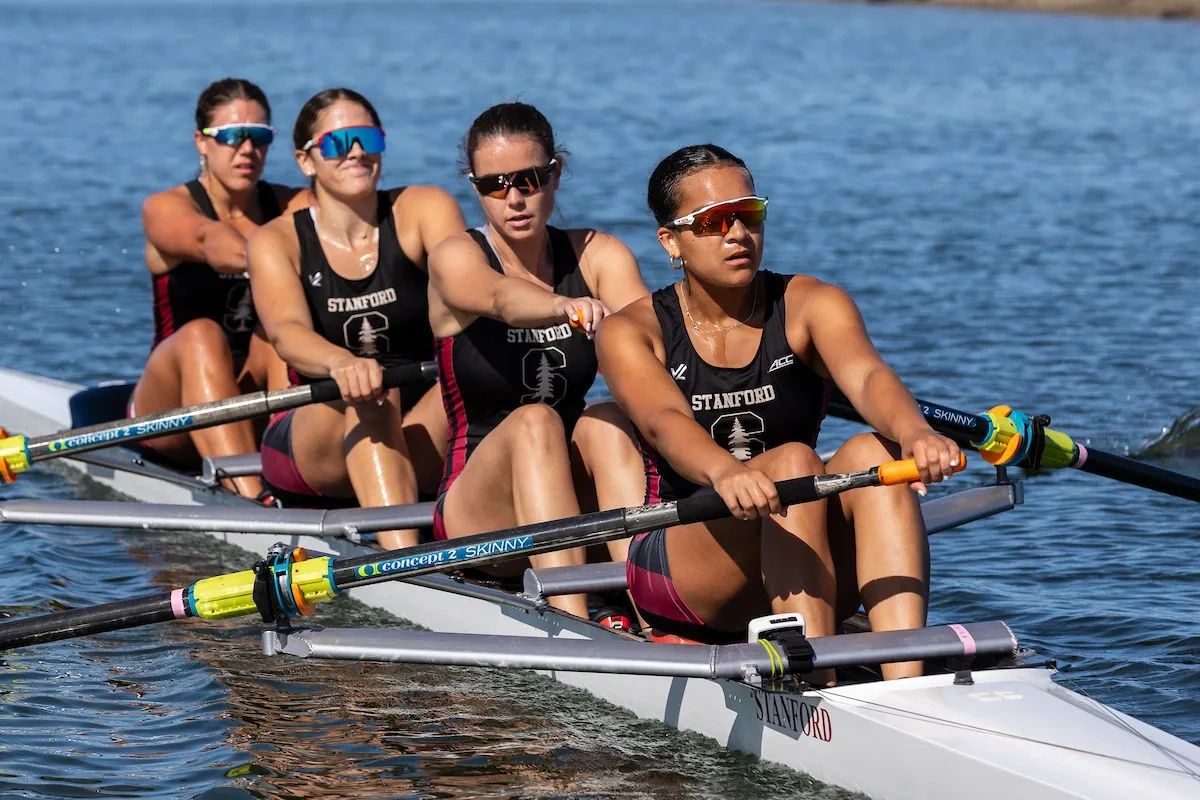 Four female rowers from Stanford team rowing intensely on water.