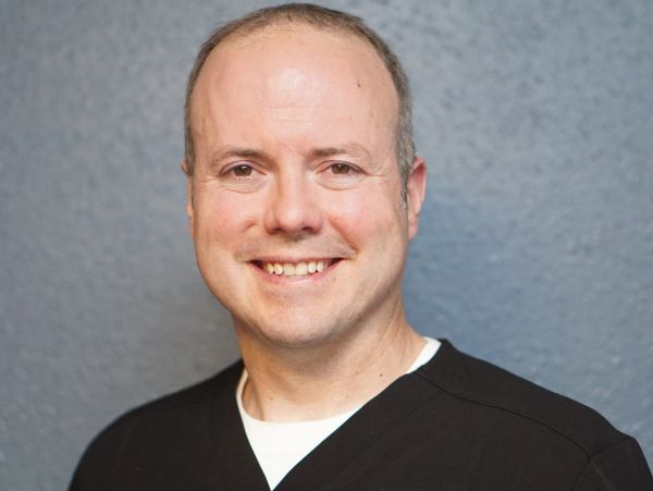 Smiling man in black shirt against gray background.