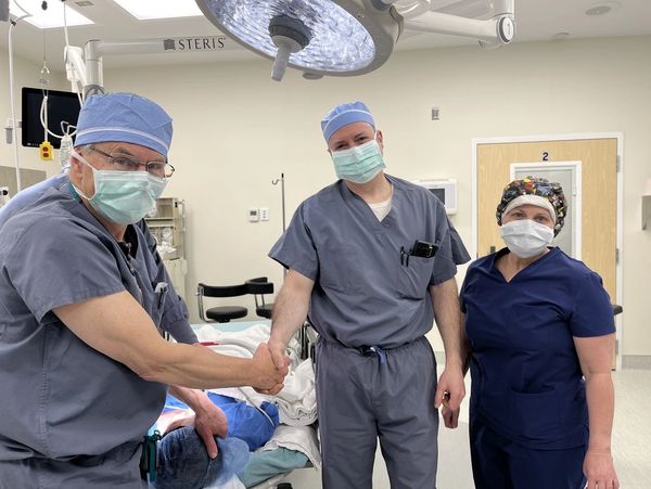 Medical team in scrubs shaking hands in hospital room.