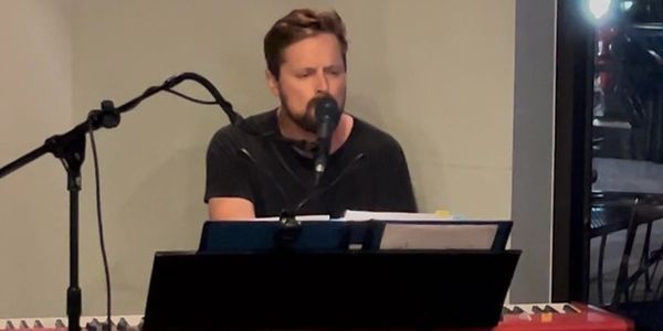 Man singing and playing a keyboard in an indoor setting.