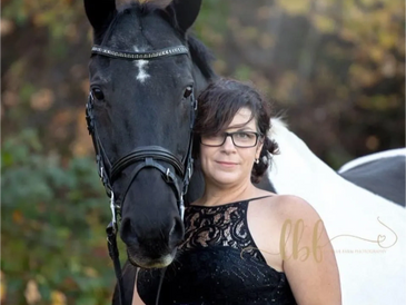 Woman in black dress posing with a black horse outdoors.